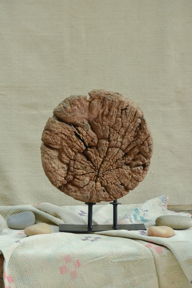 Ekaurr Aakhar circular okhali mortar base with concentric weathered cracks repurposed as a grounding sculptural decor piece on an iron stand, raw heritage home accent for consoles and shelves