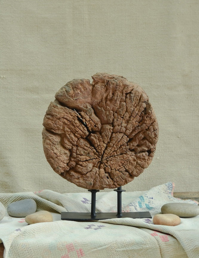 Ekaurr Aakhar circular okhali mortar base with concentric weathered cracks repurposed as a grounding sculptural decor piece on an iron stand, raw heritage home accent for consoles and shelves