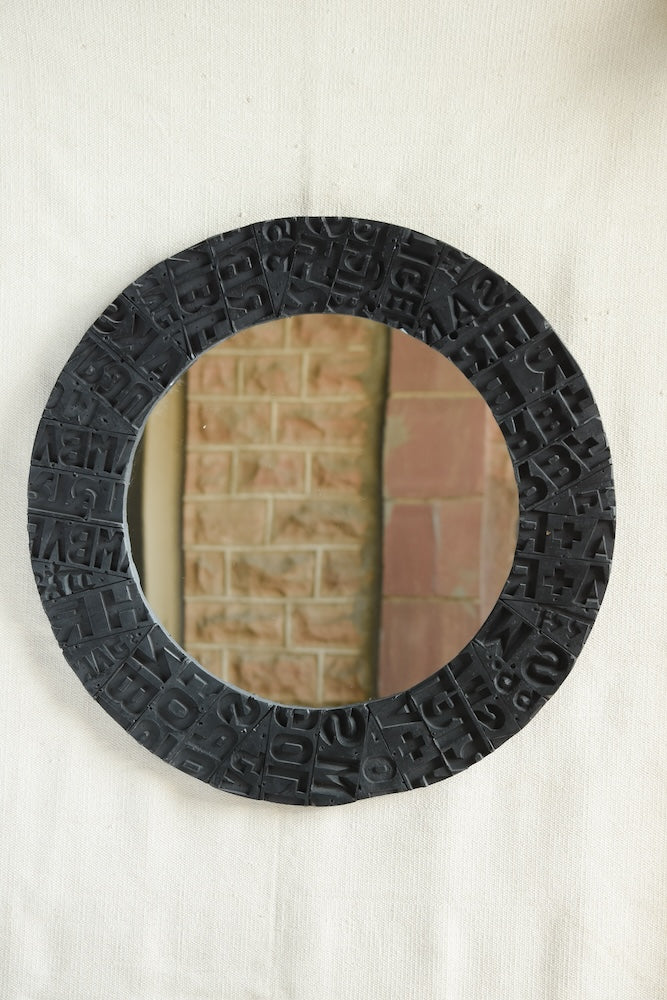 Ekaurr Artisan Wooden Emblem Round Mirror with sculptural border of black-finished carved wooden emblem blocks showing abstract motifs and typographic impressions
