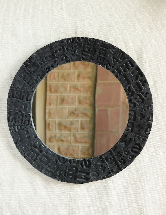 Ekaurr Artisan Wooden Emblem Round Mirror with sculptural border of black-finished carved wooden emblem blocks showing abstract motifs and typographic impressions