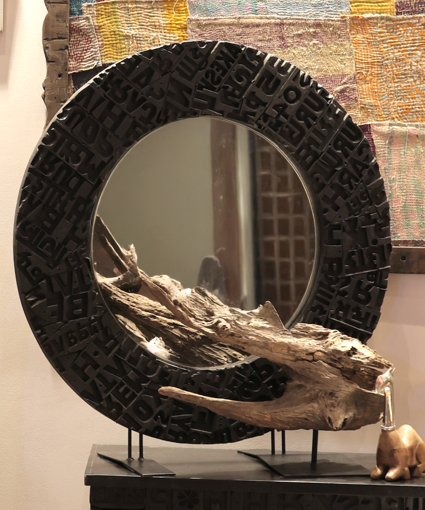 Ekaurr Artisan Wooden Emblem Round Mirror shown in styled setting, handcrafted 30-inch round mirror with dimensional black emblem frame for living room or entryway wall