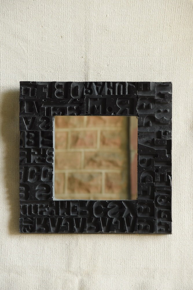 Ekaurr Artisan Wooden Emblem Square Mirror framed with black-finished vintage wooden emblem blocks featuring abstract letterforms and carved symbols, handcrafted heritage wall mirror